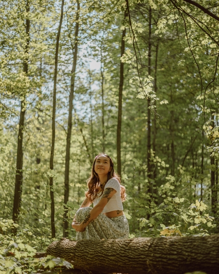 Girl sitting down next to a log in a woodland