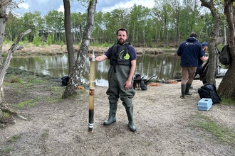 Ben standing with a core sample next to a large pond