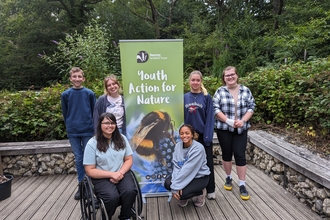 Group of young people stood smiling around a "Youth Action for Nature" banner