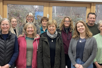Large group of smiling volunteers inside in front of a woodland background through the window