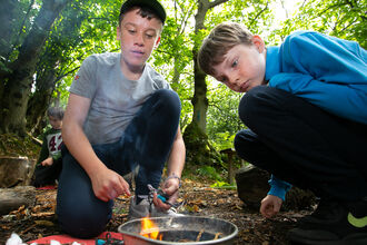 Boys lighting a fire at a woodland camp
