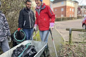 Two community members, one with a wheelbarrow, doing a litter pick
