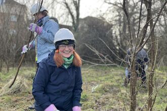 A lady smiling at the camera while clearing scrub in an urban greenspace