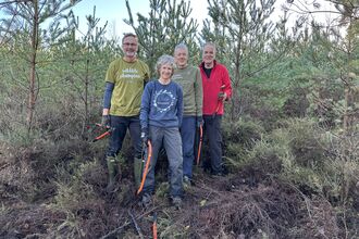A group of volunteers holding bow saws in front of pine trees 
