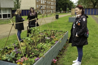 three people standing around a raised bed filled with flowers. 