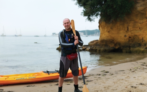 Dan stands on a beach with his kayak