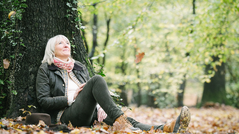 A woman leaning against a tree in the woods