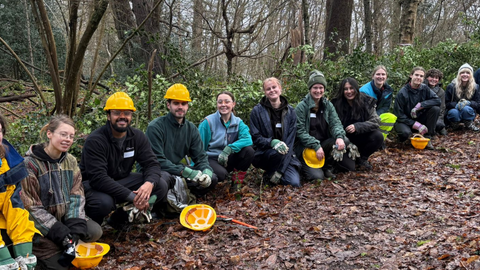 A line of young volunteers crouching on the floor with helmets and tools during a youth action volunteer day