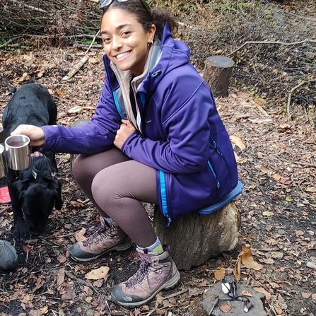 Vanessa Beal who is a placement student at Surrey Wildlife Trust, sits on a tree stump and smiles at the camera.