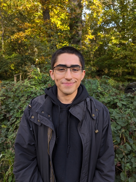 Young man stood in a natural setting smiling at the camera head on