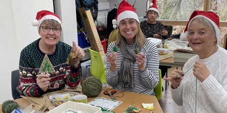 Four volunteers sat crafting activity resources, wearing Santa hats