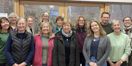 Large group of smiling volunteers inside in front of a woodland background through the window