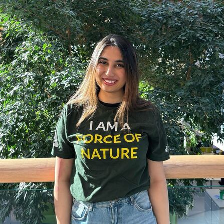Member of staff stood smiling in front of a background of greenery