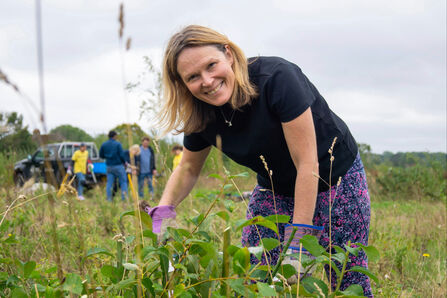 Volunteer smiling at the camera in amongst foliage on a grassland reserve