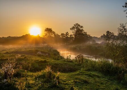 The sun rising over a river, mist drifting over the landscape