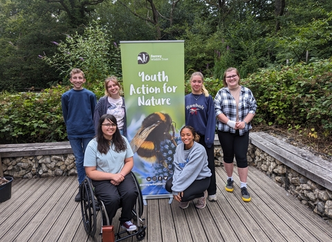 Group of young people stood smiling around a "Youth Action for Nature" banner