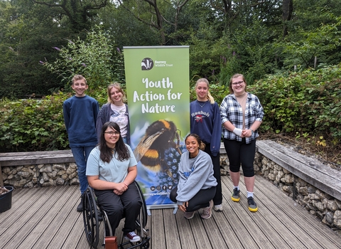 Group of young people stood smiling around a "Youth Action for Nature" banner