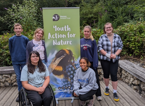 Group of young people stood smiling around a "Youth Action for Nature" banner