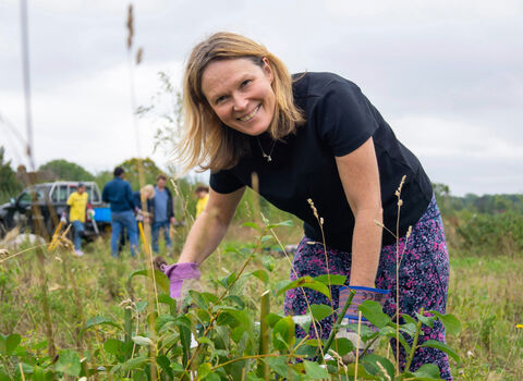 Volunteer smiling at the camera in amongst foliage on a grassland reserve